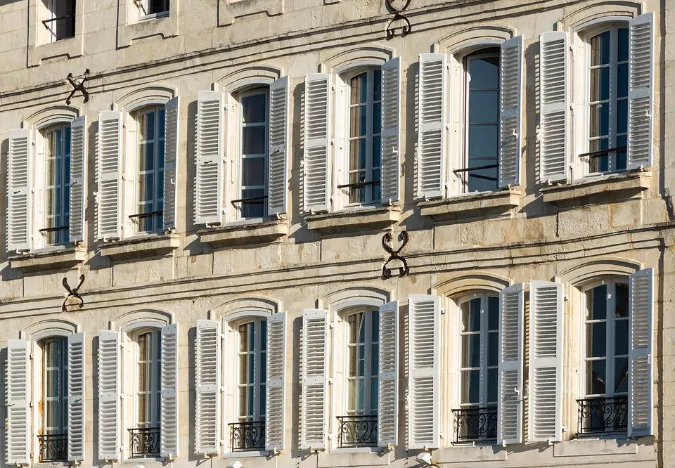 Façade en pierre de la maison Nicolas Baudin à Saint-Martin-de-Ré, avec deux rangées de fenêtres à petits carreaux encadrées de volets persiennés clairs.