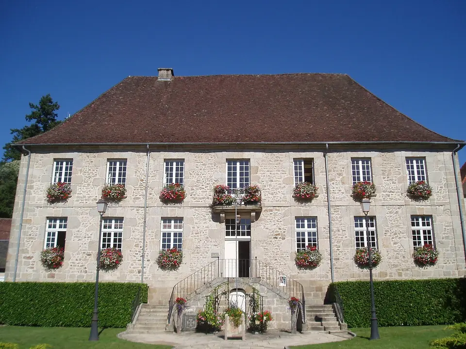 Mairie de Felletin, grande façade en pierre de taille percée de fenêtres à petits carreaux garnies de jardinières fleuries.