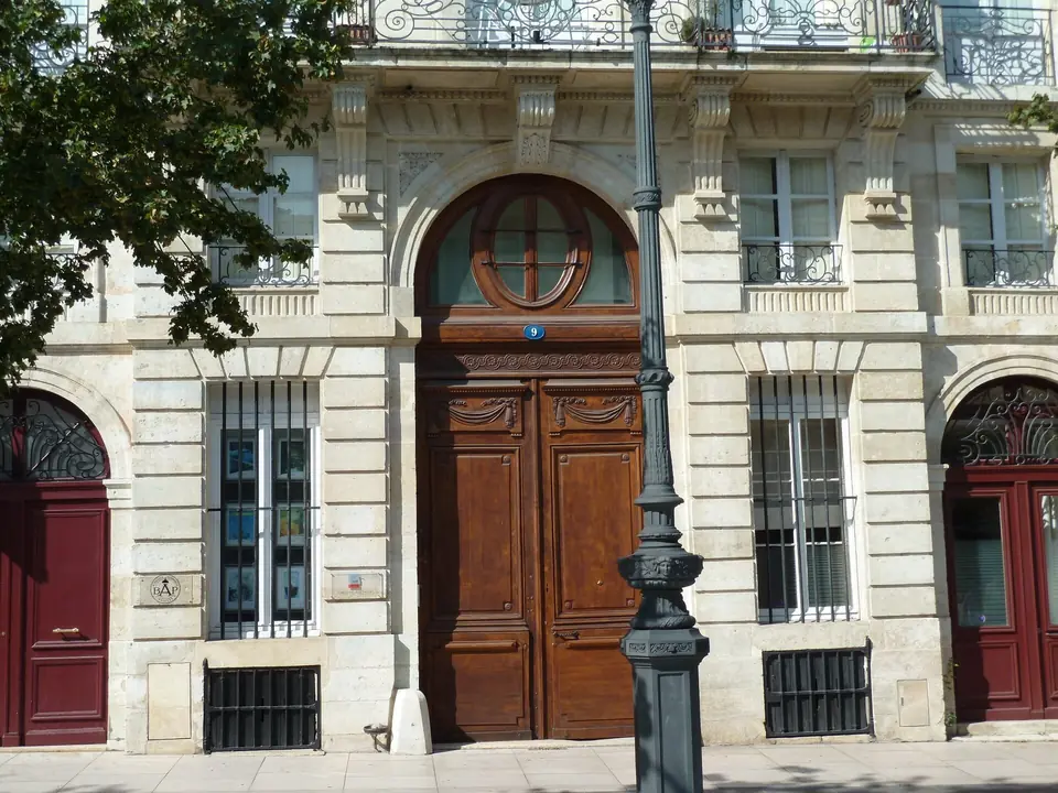 Porte d'entrée en bois mouluré à deux vantaux surmontée d'une imposte cintrée, dans une façade en pierre de taille de Bordeaux.
